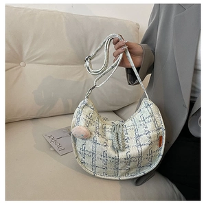 Détail du sac croissant en tweed bleu et blanc avec étiquette mode et breloque peluche