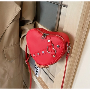 Detail view of red heart-shaped bag with silver rivets and buckle on a beige coat