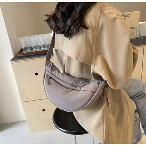 Detailed view of gray fabric crescent crossbody bag worn by model in minimalist setting