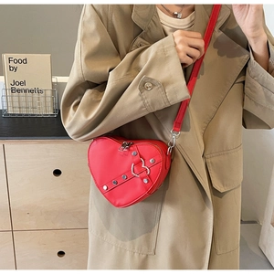 Detail view of heart-shaped red PU leather crossbody bag with silver metal studs and strap