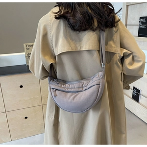 Dettaglio della borsa a mezzaluna grigio-viola con tracolla larga regolabile indossata dal modello