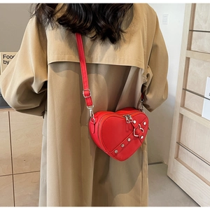 Red heart-shaped crossbody bag with stud details shown on a model in beige coat