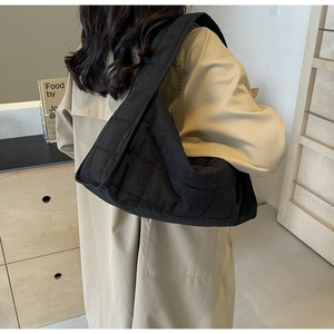 Detail of a black quilted puffer tote bag with thick strap on a beige trench coat