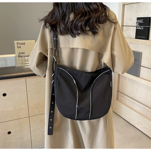 Detail of black nylon crossbody bag with silver zippers and wide strap worn by a model
