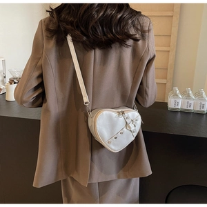Detail of heart-shaped crossbody bag with metal rivets on a textured PU leather finish