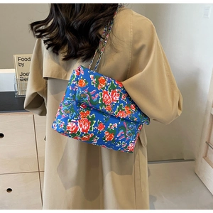 Detail of blue floral canvas shoulder bag with silver chain strap on khaki trench coat