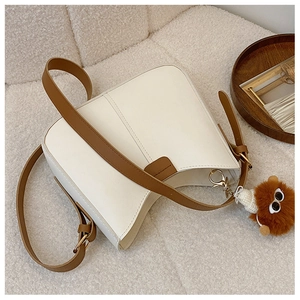 Minimalist white leather tote bag with brown straps and cute teddy charm on fabric background