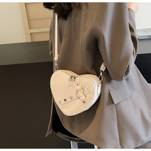 Cream heart-shaped crossbody bag with metal rivets and adjustable strap shown on model