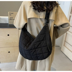Detail of black quilted nylon crescent crossbody bag worn over a beige trench coat