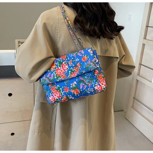 Detail of floral canvas crossbody bag with colorful woven chain strap on khaki trench coat