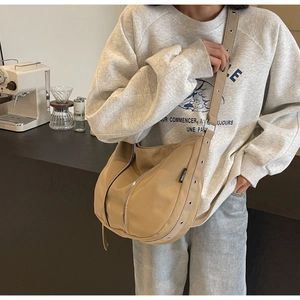 Detail of khaki nylon half-moon crossbody bag with silver zippers and metal eyelet strap