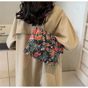 Detailed view of floral canvas shoulder bag with silver chain strap on khaki trench coat