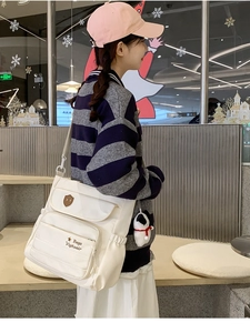 Dettaglio borsa a tracolla beige in nylon con tasca a zip e ciondolo a cucciolo