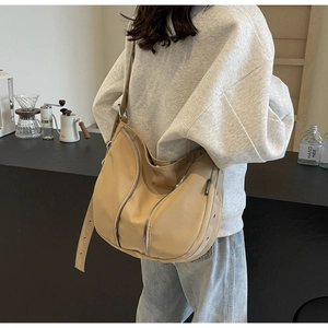 Detail of khaki hobo bag with adjustable wide strap and decorative zippers in urban setting