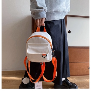 Détail d'un mini sac à dos en toile blanche avec bretelles et poignées en nylon orange vif