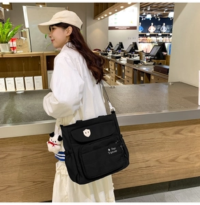 Dettaglio laterale della borsa a tracolla in nylon nero con tasche e ciondolo peluche