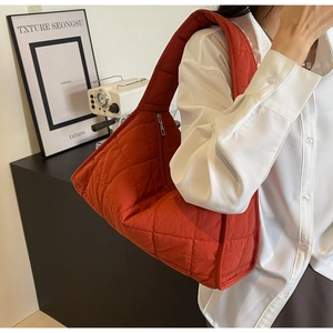 Quilted orange crossbody bag shown on model with wide shoulder strap and curved design