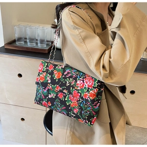 Detail of vintage floral canvas crossbody bag with elegant silver chain strap worn on coat