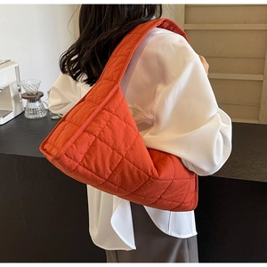 Detail of orange quilted puffer shoulder bag in a modern minimalist cafe setting