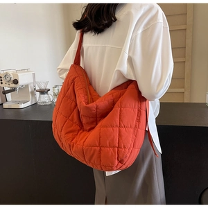 Detail of the large orange quilted puffer tote bag with wide shoulder strap worn by model