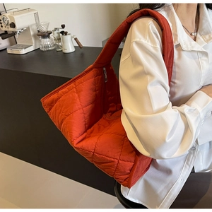 Detailed view of the orange quilted puffer bag with crossbody strap on a white shirt