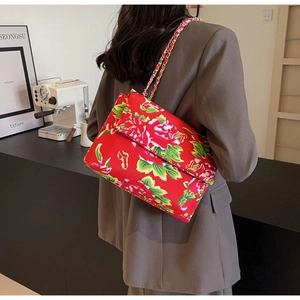Detail of red floral canvas crossbody bag with gold chain strap worn by a model