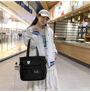 Dettaglio della borsa tote in nylon nero con multitasche e un ciondolo a forma di cucciolo