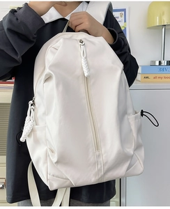 Detail of white nylon backpack featuring vertical zipper and decorative woven puller