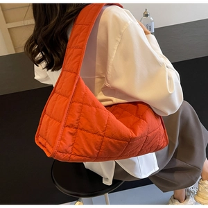 Rear view of model wearing a bright orange quilted hobo bag in soft nylon fabric