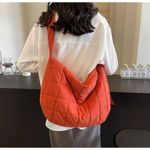 Detail showing the orange quilted nylon crossbody bag texture and large diamond stitching