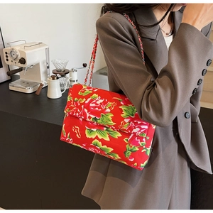 Detail of red floral peony canvas shoulder bag with silver metal chain strap on a model