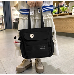 Dettaglio della borsa tote in nylon nero con tasche frontali e ciondolo a forma di cucciolo
