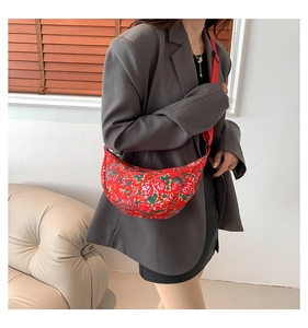 Detail shot of a red floral nylon crescent crossbody bag worn over a grey blazer jacket