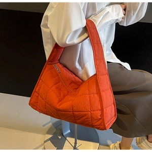 Detail of orange quilted shoulder bag with large diamond stitching and sleek metal zipper
