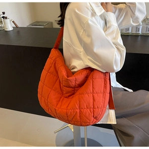 Close-up of bright orange quilted puffer bag with crossbody strap on a casual model