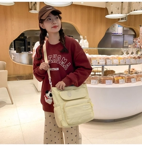 Dettaglio borsa a tracolla in nylon crema con multitasche e ciondolo a panda