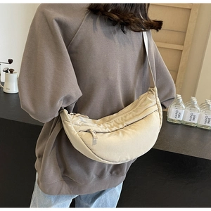 Borsa a tracolla a mezzaluna in nylon beige indossata da una modella per un look casual