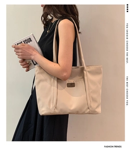 Close-up of beige canvas tote bag with brown leather logo patch on model's shoulder