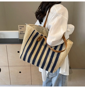 Close-up of woven straw tote bag with navy stripes and brown leather shoulder straps