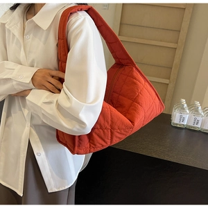 Quilted burnt orange puffer shoulder bag shown with a model in a minimalist lifestyle setting