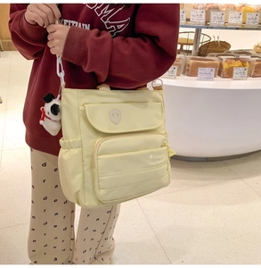 Dettaglio della borsa a tracolla in nylon crema con design multitasche e ciondolo a forma di cane