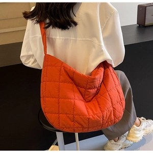 Rear view of model wearing a large orange quilted crossbody bag with diamond patterns