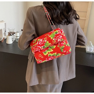 Detail of red floral canvas crossbody bag with chain strap on a modern cafe background