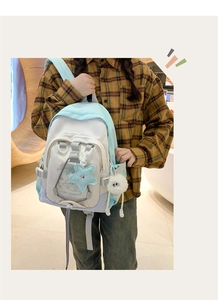 Close-up of stylish tricolor nylon backpack with star pendant and fuzzy ball on model