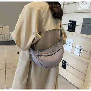 Close-up of a crescent nylon crossbody bag worn with a classic khaki trench coat