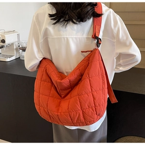 Detail of orange quilted puffer crossbody bag with wide shoulder strap worn by a model