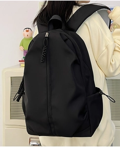 Detail of minimalist nylon backpack showing vertical zipper pocket and drawstring side pouch