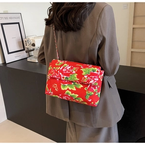 Detail of red floral canvas crossbody bag with metal chain strap on grey blazer