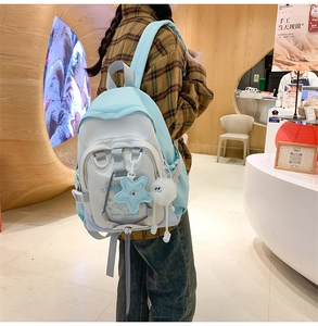Side view of a light blue and white nylon backpack featuring star and pompom charms