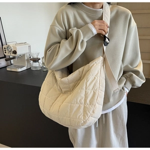 Minimalist beige quilted crescent crossbody bag with adjustable wide shoulder strap detail
